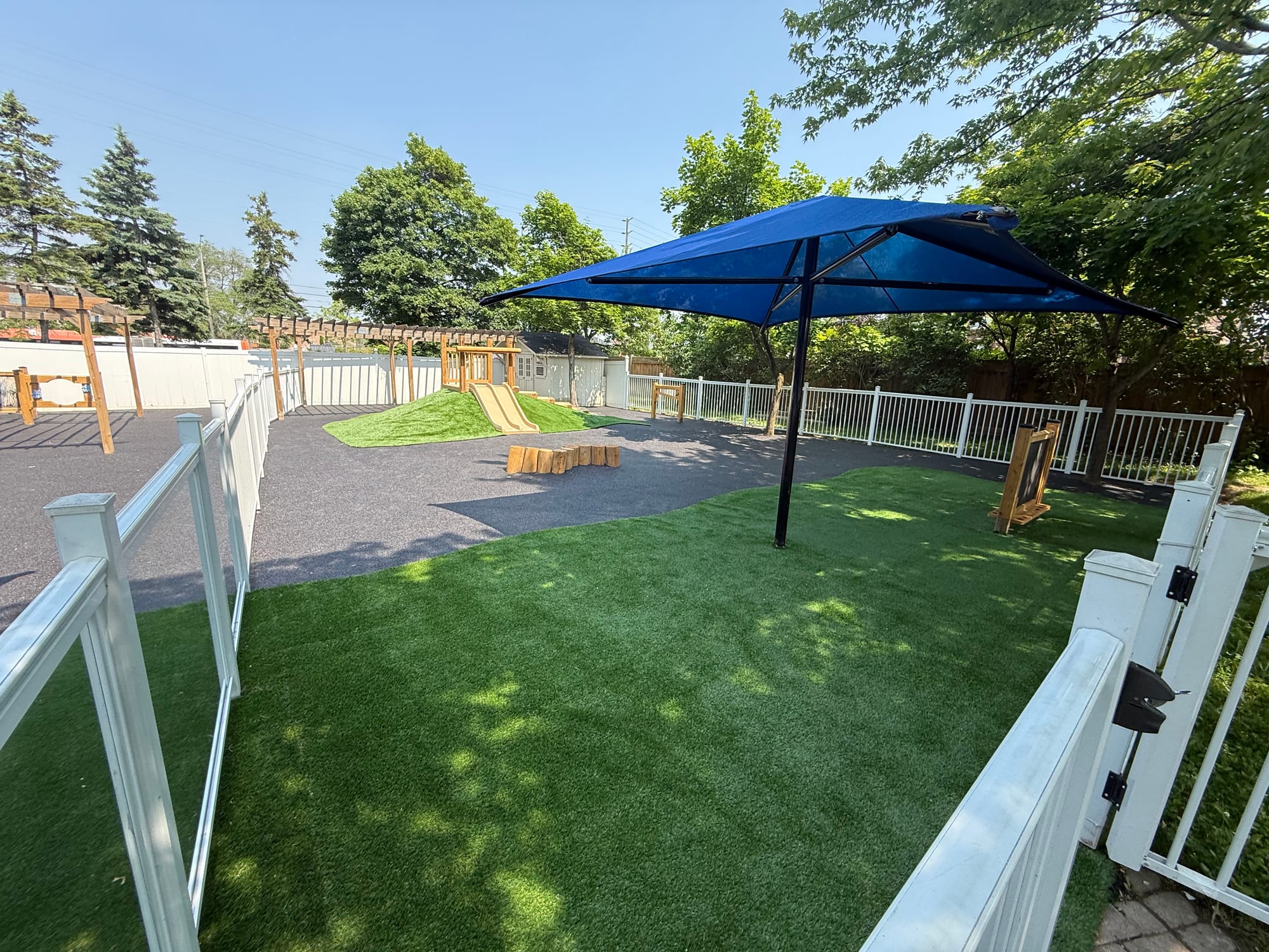 Daycare play space with rubber surfacing, turf and a blue shade