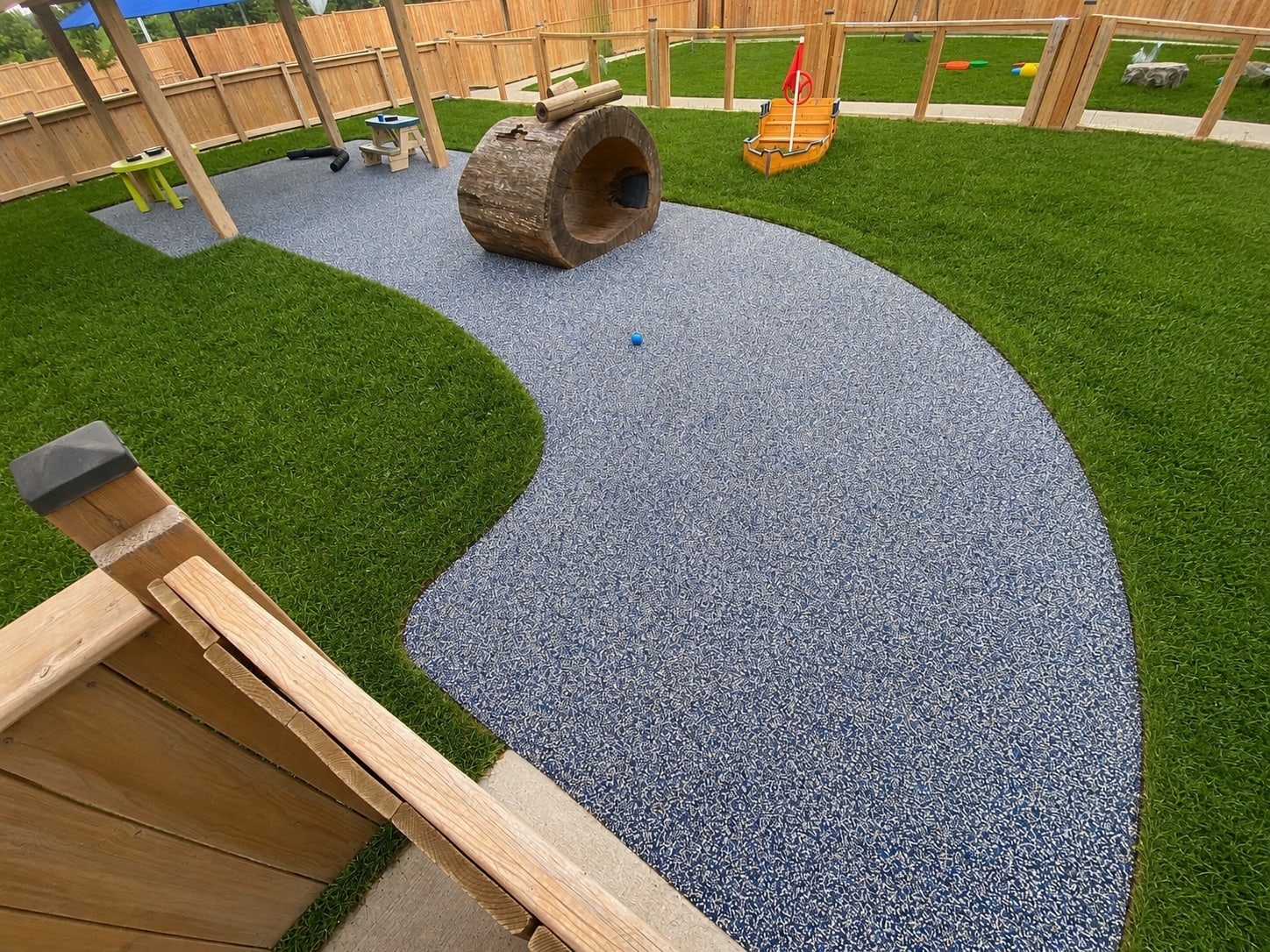 Rubber playground surface with turf and log structure